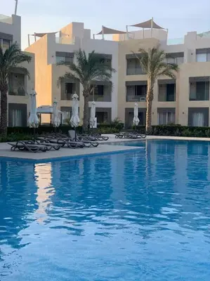 a swimming pool with chairs and umbrellas and a building at Mangroovy - 1BR GF +2 wall beds Garden & Pool view in Hurghada