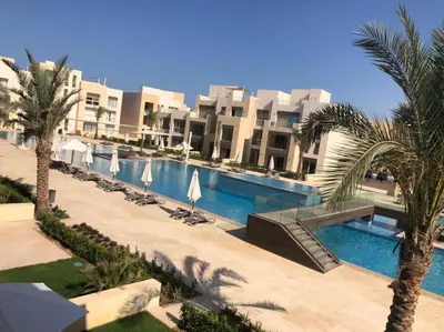 a resort with a swimming pool with palm trees and buildings at Mangroovy - 2BR La Blanca Pool View in Hurghada