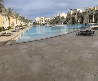 a large swimming pool with chairs and palm trees and buildings at Mangroovy Comfy 2 Bedroom in Hurghada